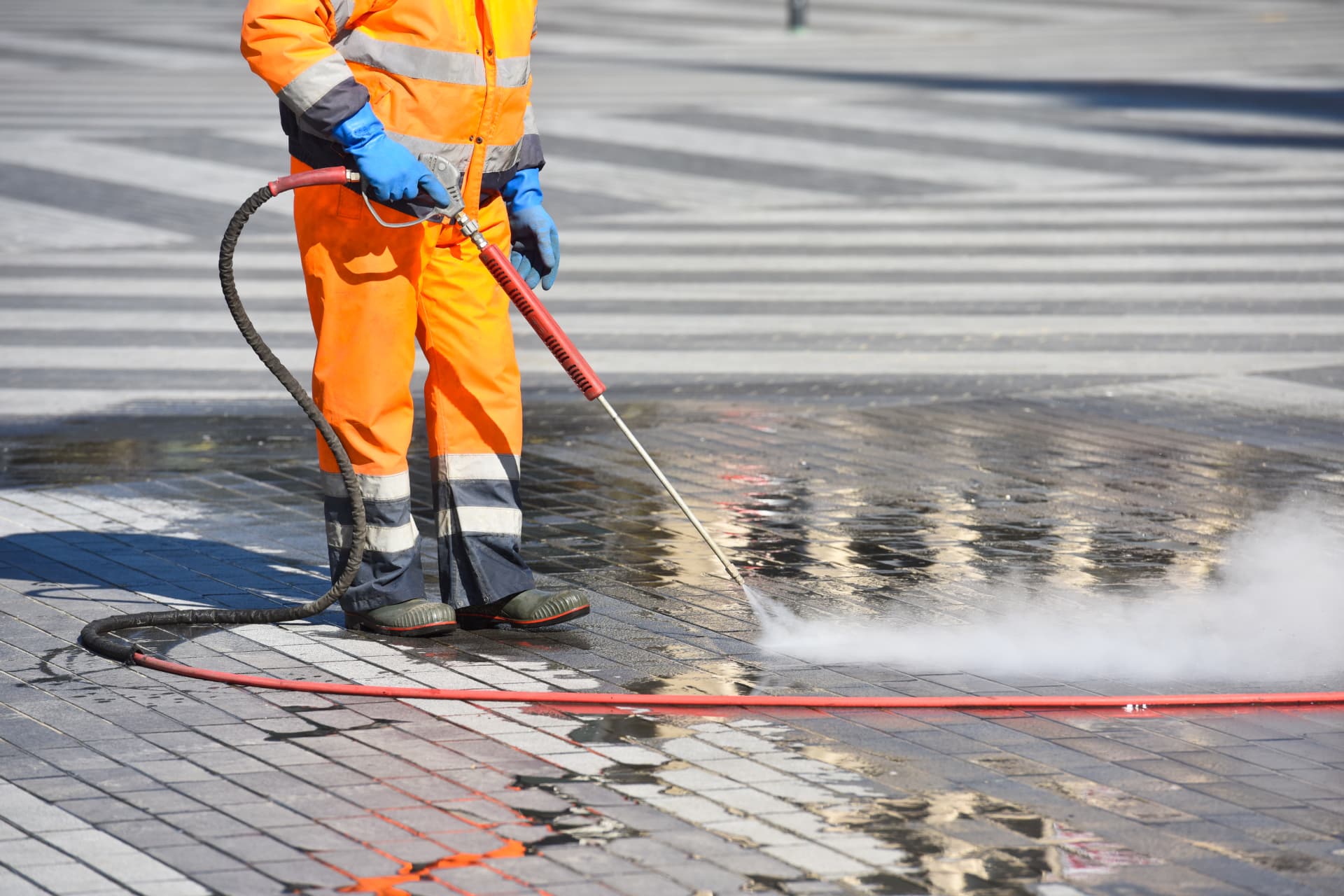 Technicien en habit haute visibilité lavant à haute pression un pavé de béton