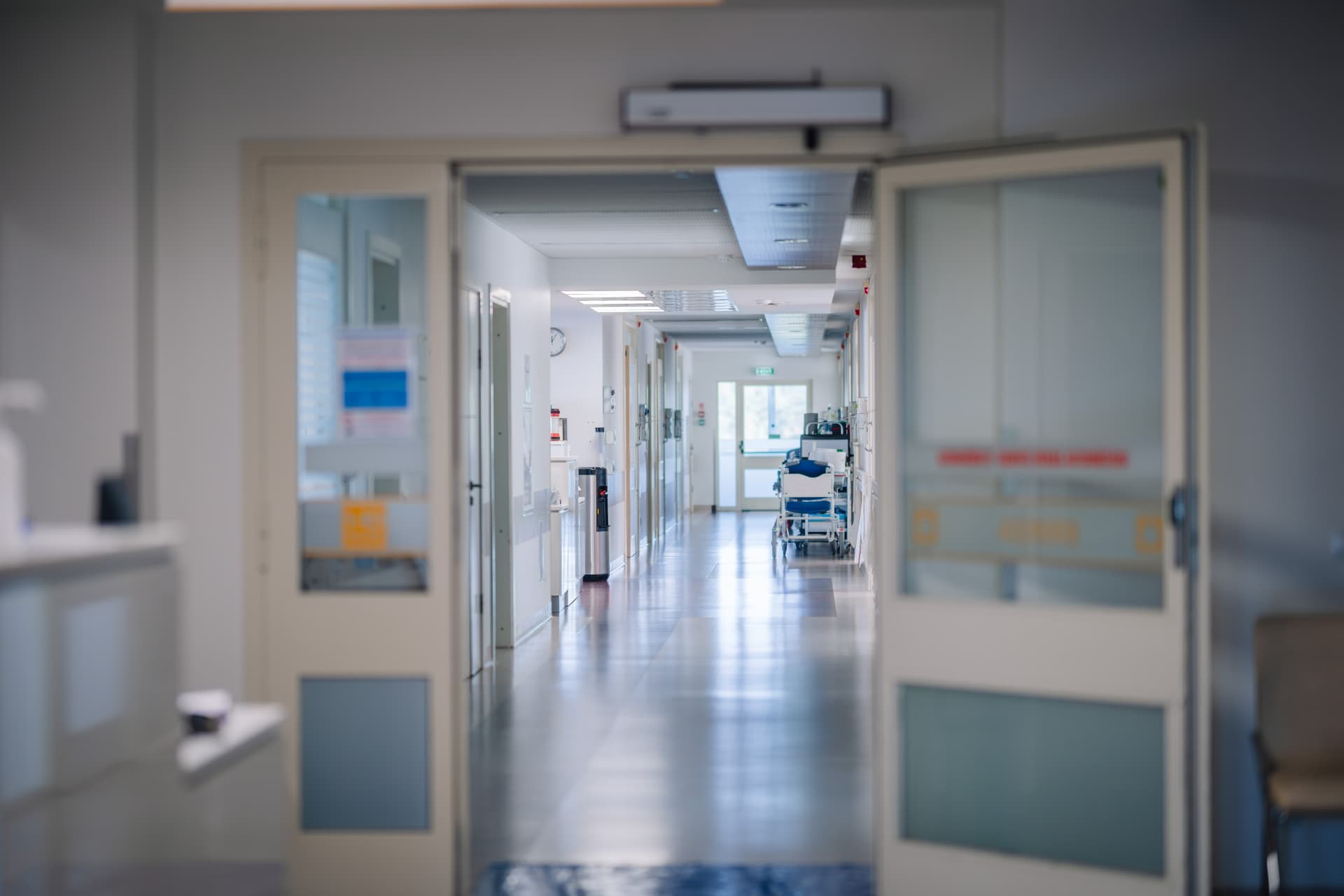 Corridor d'unité de soins aux portes ouvertes, surfaces lisses et civière au fond